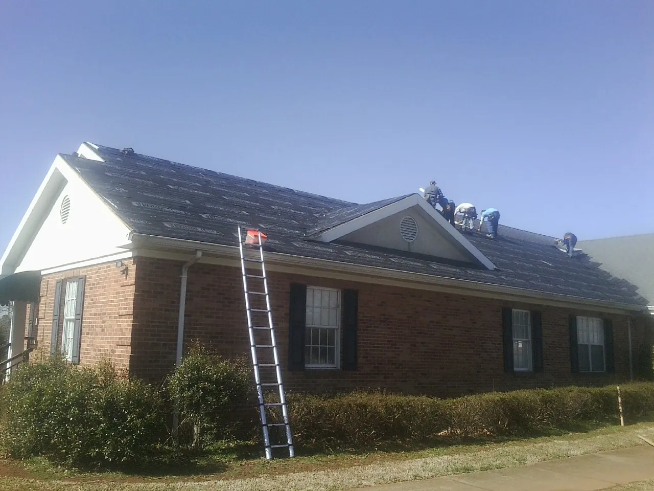 Crew tearing shingles off a brick ranch roof with a ladder set — Metal Roof Repair work by our crew in North Branch