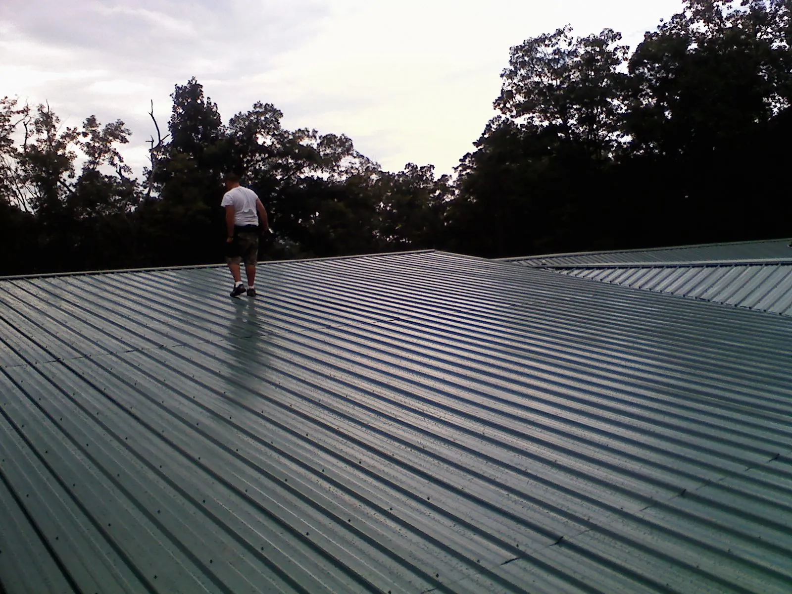 Roofer walking a wide expanse of new green metal roofing in North Branch